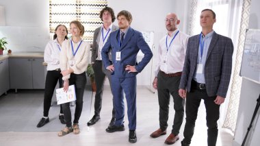 Ekonomistler ve finansörlerden oluşan profesyonel bir ekip. Bir danışmanlık firması. Takım elbiseli bir grup kadın ve erkek konferans odasında dikiliyorlar. Olay yeri profesyonelce işlenmiş.