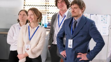 İş kıyafetleri içinde mutlu bir erkek ve kadın öğrenci grubu odada duruyor. Hepsinin göğsünde isim etiketi var. Sahne profesyonel ve ciddi.