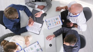 Yönetim, sözleşmenin detaylarını, üst görüşü tartışıyor. Bir grup iş adamı kağıt ve dizüstü bilgisayarlarla bir masada oturuyor. Önemli bir işlemin sonucu.