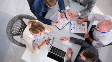 Beş başarılı profesyonel pazarlamacı, kağıtları ve dizüstü bilgisayarı olan bir masada oturuyor. Birlikte bir proje üzerinde çalışıyorlar, içlerinden biri elinde kalem tutup grafiği işaret ediyor..