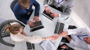 Bir grup insan dizüstü bilgisayarlı ve kontratlı bir masada el sıkışıyor. Bir anlaşma yapıyorum. Sahne profesyonel ve işbirlikçi. Takım çalışması.