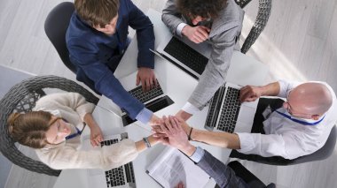 Takım çalışması ve şirket birliği kavramı. Takım oluşturma. Bir grup girişimci dizüstü bilgisayarlarla bir masada oturuyor ve avuçlarını meslektaşlarının avuçlarına koyuyorlar..