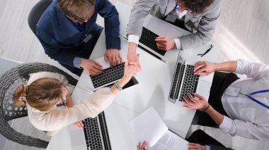 İş adamları dizüstü bilgisayarlarla dolu bir masada oturuyorlar. El sıkışıyorlar ve birlikte çalışıyorlar. İyi bir anlaşma. Selamlar. Toplantıda çalışma saatleri