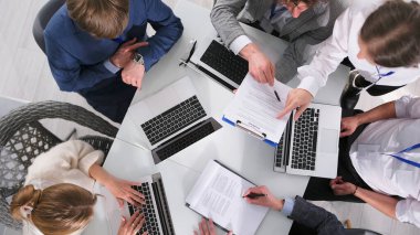 Patronun özel asistanı kontratta dikkat etmeniz gereken ayrıntılara dikkat çekiyor. Bir grup insan dizüstü bilgisayarlarla ve iş belgeleriyle bir masada oturuyor.