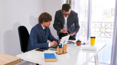 Pazarlama bölümünün başı patronla tabletteki logonun tasarımını koordine ediyor. Takım elbiseli iki adam önemli bir şey tartışıyorlar..