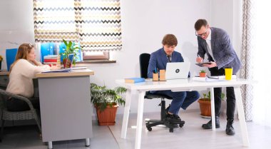 Patron, bir masada dizüstü bilgisayarla oturan kişisel asistanına talimat verir. Yanında sıkılmış bir sekreter oturuyor. Aile ofisi. Çalışma günleri