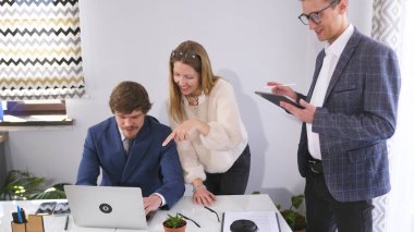 Masanın etrafında dizüstü bilgisayarı açık duran üç mutlu insan var. Diğer ikisi aksiyonu izlerken kadın tasarımcı ekranı işaret ediyor. Sahne odaklandı.