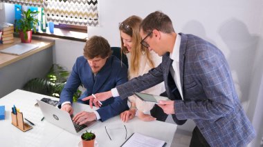 Profesyonel pazarlamacılardan oluşan bir ekip müdürün masasında toplantı yapıyor. İki erkek ve bir kadın dizüstü bilgisayara bakıyor. Adam ekranı parmağıyla işaret ediyor.. 