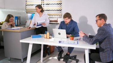 Bir grup genç iş adamı ortak bir amaç için birlikte çalışıyorlar. İki işadamı bir dizüstü bilgisayar ve tabletle bir masada oturuyorlar. Kadınlar birbirleriyle iletişim kurarlar..