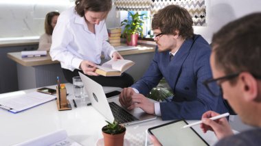 Bir grup öğrenci bir dizüstü bilgisayar, bir kitap ve bir tabletle bir masada oturuyor. Girişimlerini tartışıyorlar. Genç iş adamları birlikte çalışır. Aile Ofisi