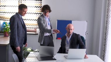 Şirketin avukatı ve finansörü patrona yeni bir proje için tavsiyede bulunuyor. Üç iş adamı bir dizüstü bilgisayara bakarken önemli bir müşteriyi tartışıyor..