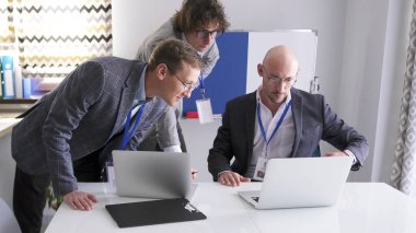 Üç adam bir dizüstü bilgisayar ekranına bakarak borsa hareketlerini takip ediyor. Bir grup ekonomist pazar durumunu analiz ediyor. Sahne profesyonel ve odaklı.