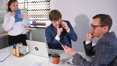 Mavi takım elbiseli ve gözlüklü ciddi bir adam telefonda konuşuyor ve ona iş arkadaşlarını rahatsız etmemesini söylüyor. İki adam bir masada oturuyor ve sekreter ürkmüş ve günlüğünü tutuyor..