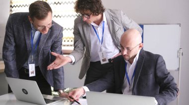Takım elbiseli ve gözlüklü üç adam konferans odasında toplantı yapıyor. İş adamları dizüstü bilgisayarlara bakıp ortak bir proje üzerinde çalışıyorlar. Takım çalışması. Takım oluşturma