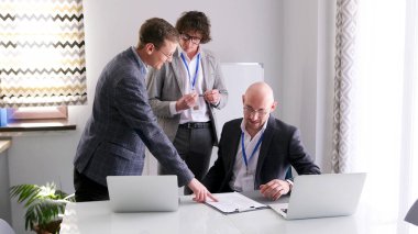 Bir grup adam sözleşmenin detaylarını tartışıyor. Adamlardan biri önündeki kağıtta bir şeye işaret ediyor. Sahne odaklı ve ciddi.