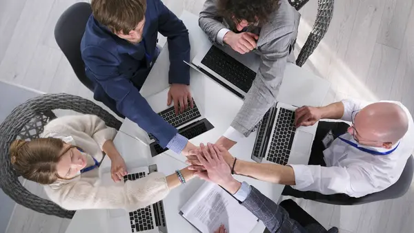 Takım çalışması ve şirket birliği kavramı. Takım oluşturma. Bir grup girişimci dizüstü bilgisayarlarla bir masada oturuyor ve avuçlarını meslektaşlarının avuçlarına koyuyorlar..