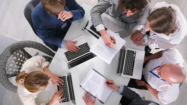 Şirketin kurucusu yönetim kurulu toplantısında önemli bir belgeyi imzalar. Astları laptoplarla dolu bir masada onun yanında oturuyorlar.