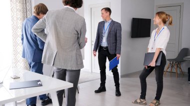 Bir grup girişimci bir konferans odasında duruyor ve günün planlarını tartışıyorlar. Birbirleriyle konuşuyorlar ve ellerinde kağıtlar tutuyorlar. Sahne profesyonel ve ciddi.