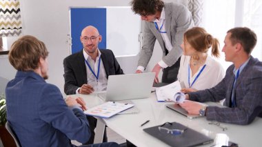 Başarılı, kendinden emin iş adamları ve girişimciler konferans odasında bir brifing düzenliyor. Bir grup ofis çalışanı ellerinde laptop ve kağıtlarla bir masada oturuyorlar. Sahne profesyonel ve ciddi.