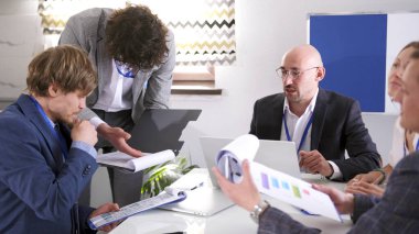 Bir grup analist, bir şirketin kriz anındaki gelişim stratejisi hakkında fikir alışverişinde bulunuyor. Meslektaşlar kağıt ve dizüstü bilgisayarlarla dolu bir masada oturuyorlar. Toplantı ya da bilgilendirme