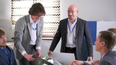 İşlemin başarıyla tamamlanması. Şirketlerin başkanları önemli bir anlaşma imzaladılar. Bir grup ofis çalışanı açık bir dizüstü bilgisayarla bir masada çalışıyor. Hepsi takım elbise giyiyor..