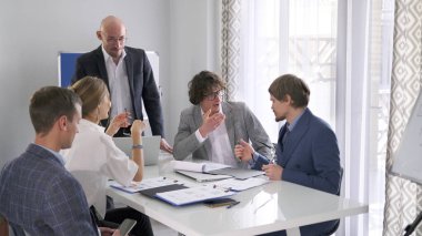 Bir grup insan konferans odasında bir masada oturuyor. Hepsi iş kıyafetleri giymişler ve yeni bir iş projesini tartışıyorlar. Takım oluşturma ve işbirliği
