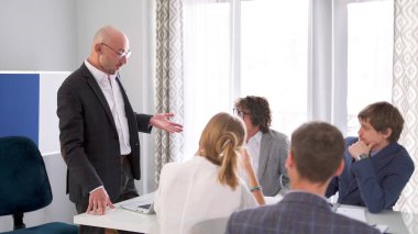 İş adamı gibi, kendinden emin bir adam konferans odasında bir grup insanın önünde sunum yapıyor. Bir grup kurucu masaya oturur ve bir akıl hocasını dinler. Sabah planlama oturumu