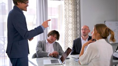 Gülümseyen bir adam bir grup insanın önünde sunum yapar. Akıl hocası mavi bir takım elbise ve gözlük takıyor. Şirket personeli dizüstü bilgisayar ve kağıtlarla dolu bir masada oturuyor. Sahne profesyonel ve odaklı.