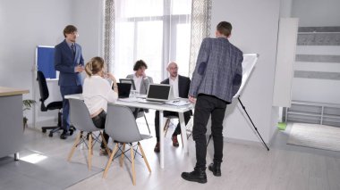 Brifingde sunum. Bir grup insan konferans odasında bir masanın etrafında toplandı. Buradaki atmosfer profesyonel ve önemli konuları tartıştıkları için odaklanmış durumda..