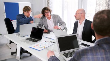 Şirketin kurucularıyla toplantı. Gözlüklü ve takım elbiseli bir grup adam dizüstü bilgisayar ve belgelerle bir masada oturuyorlar. Bir adam beyaz tahtadaki bir şeyi işaret ediyor. Sabah planlama oturumu