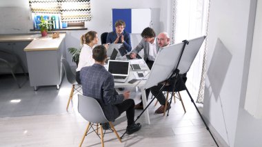 Bir grup iş adamı bir ofis masasında oturuyor. Mini konferans. Takım oluşturma ve işbirliği. Hepsi ortak bir proje üzerinde çalışıyor..