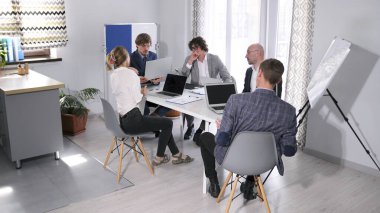 Bir grup girişimci konferans odasında dizüstü bilgisayarlarla bir masada oturuyor. Sahne profesyonel ve odaklanmış, şirketin kurucuları iş ile ilgili konuları tartışıyor.