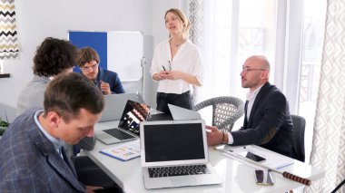 Bir grup finansör dizüstü bilgisayarlarla bir masada oturuyor ve güzel bir genç kadın bir sunum yapıyor. Sahne profesyonel ve odaklanmış. Çalışma günleri