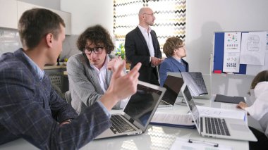 Bir grup acemi dizüstü bilgisayarları açık bir masada oturmuş bir şeyler tartışıyorlar. Sahne odaklı ve ciddi, çünkü insanlar sohbete dalmış ve dizüstü bilgisayarları üzerinde çalışıyorlar..