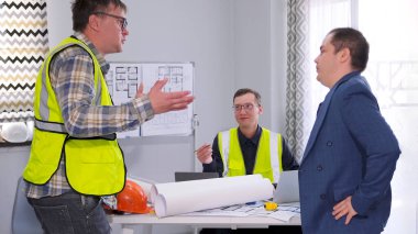 Yeşil sinyal yeleği giyen basit bir işçi yapılan işi patrona bildirir. Planlarla dolu bir masanın etrafında üç adam var. Mimarlık Bürosu. İnşaat mühendisinin ofisinde.