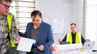 Mimarlık bürosunun ciddi ve tatminsiz başkanı, yeşil yelekli bir işçiyi mühendislik ofisinden dışarı çıkarıyor. Takım elbiseli bir işadamı fiyatına bakar. Sahne profesyonelce ve konsantrasyonla yapıldı.