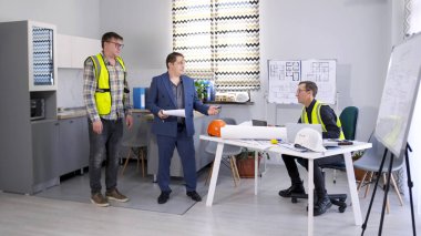 Yeşil yelekli ustabaşı projenin fiyatını arttırmak istiyor. İşadamı ve mimar mimarlık bürosunda inşaat projesinin detaylarını tartışıyor..