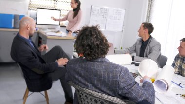 Bir grup mühendis ve mimar konferans odasında bir masada oturmuş bayan meslektaşlarının sunumunu izliyorlar. Mimarlık bürosunda brifing.