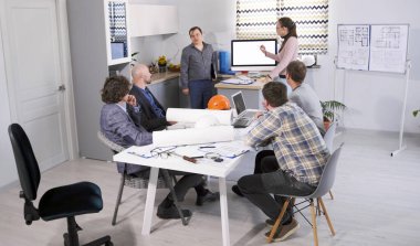 Erkek baş mühendis ve kadın yardımcısı kurucular kuruluna yeni bir mimari proje sunar. Bir grup insan sunum için rahat bir aile ofisinde bir masada oturuyor.. 