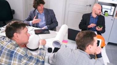 Mimarlık bürosunda brifing. Bir grup adam konferans odasında bir masada oturuyor ve bir inşaat projesini tartışıyorlar. Şirketin patronu elinde bir cep telefonu tutuyor..