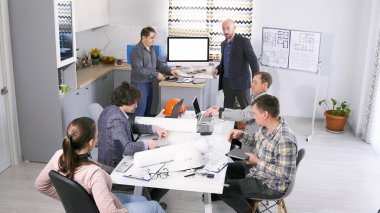 Bir grup mimar sıcak bir aile ofisinde brifing için toplandı. Alışveriş merkezinin inşaat projesini tartışıyorlar. Takım çalışması. Takım oluşturma. Sahne işbirlikçi ve odaklı.