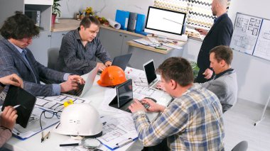 Şirketin baş mimarı yönetim kuruluna bir sunum yapacak. Bir grup adam konferans odasında bir masada oturuyor, bir inşaat projesi üzerinde çalışıyorlar. Sahne odaklandı.