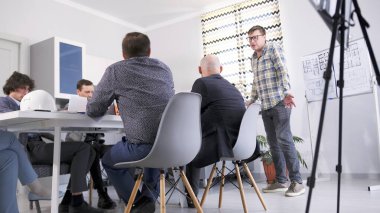 İnşaat şirketinin müteahhiti konferans odasındaki bir toplantıda müdüre rapor veriyor. Bir grup insan bir mimarlık firmasının aile ofisinde masada oturuyor..