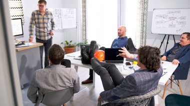 İnşaat şirketinin yönetimi yeni mimari tesisin kârlılığını ve detaylarını tartışıyor. Sunumu elinde işaret olan bir mimari mühendisi yönetiyor..