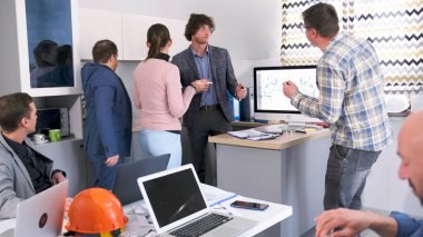 Bir grup insan bir bilgisayar monitörünün etrafında bir bina planıyla toplandı. Mimarlar, mühendisler ve inşaatçılar iş başında. Sahne işbirliği ve odaklanma için tasarlandı.