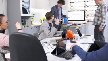 İki meslektaş mimari bir proje sunuyorlar. Okutman grubun sorularını cevaplar. İnsanlar sabah toplantısı için toplandı. Sahne profesyonel ve odaklı.