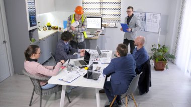 Mimarlık şirketinin kurucuları modern bir hastane inşaatı hakkında brifingde. Bir grup iş adamı sıcak bir aile ofisindeki masanın etrafında toplanıyor. İşbirliği fikri