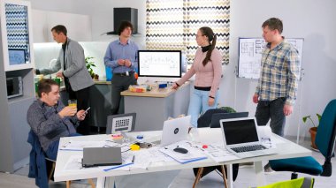 Ofis mutfağında, bir grup iş arkadaşı bir mola sırasında atıştırmak için bir masada toplandılar. Odada birkaç dizüstü bilgisayar ve saksı bitkileri var. Atmosfer sakin görünüyor.