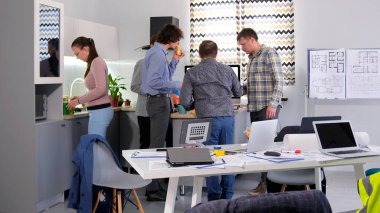 Kahve molası ya da iş yemeği. Bir grup insan aile ofisinin rahat mutfağındaki masanın etrafında toplandı. Odada birkaç dizüstü bilgisayar ve saksı bitkileri var. Atmosfer rahat.