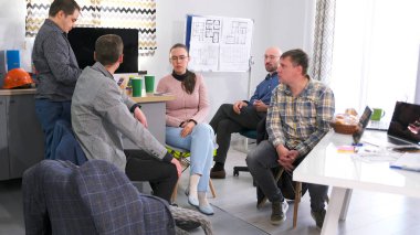 Çalışanlar son haberleri kahve molasında tartıştılar. İş yemeği. Bir grup insan konferans odasında bir masada oturuyor ve kahve içiyorlar. Mimarlık bürosundaki işine ara veriyor.